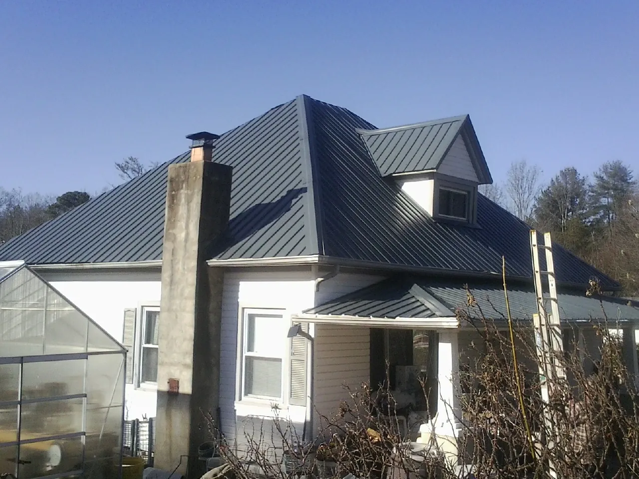 Dark blue standing seam metal roof on a white farmhouse with dormer — Slate & Tile Roof Repair by Roofing Brothers in Poolesville