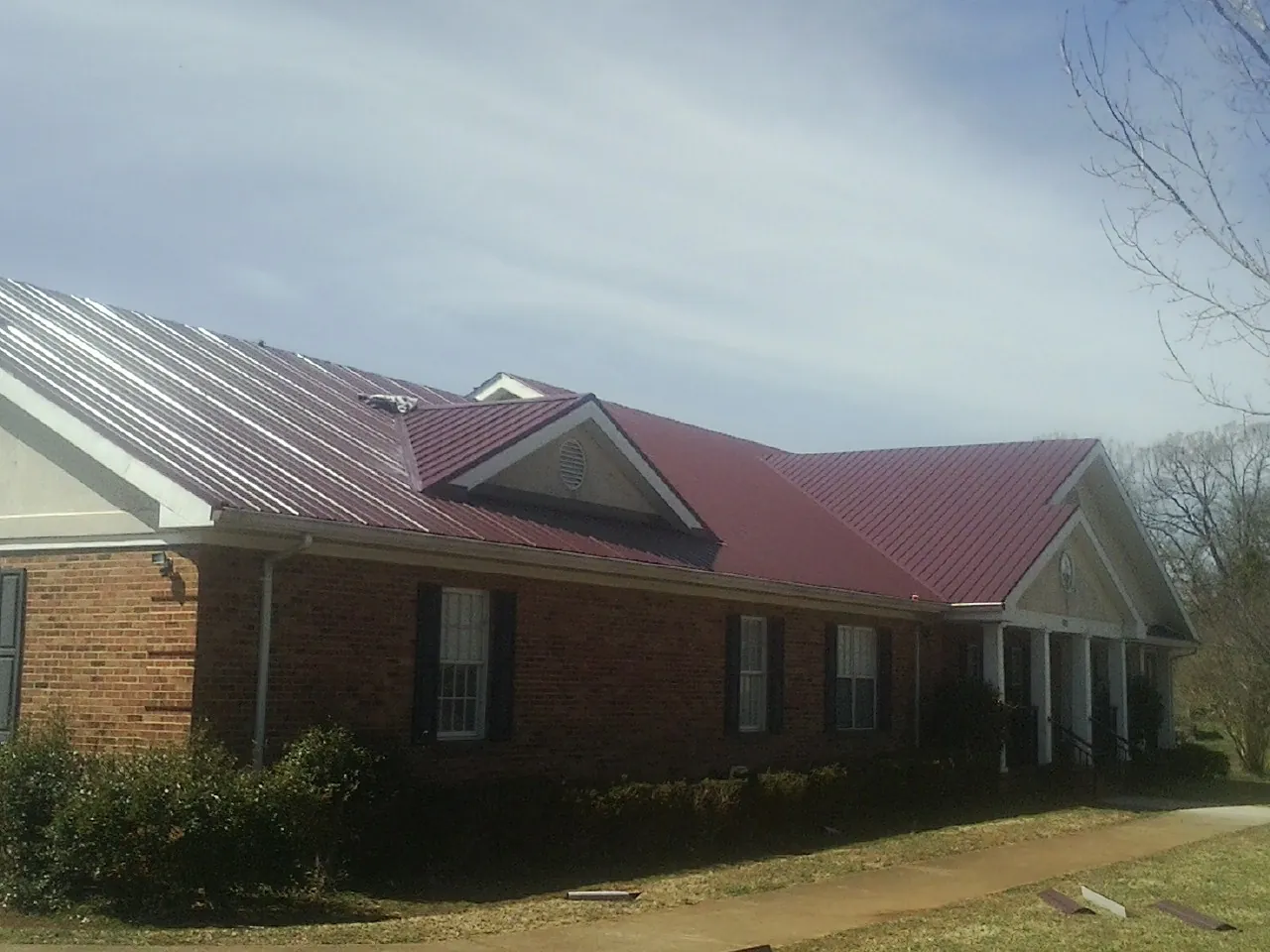 Red metal roof with gabled entries on a long brick building, from a Hail Damage Roof Repair job in Poolesville