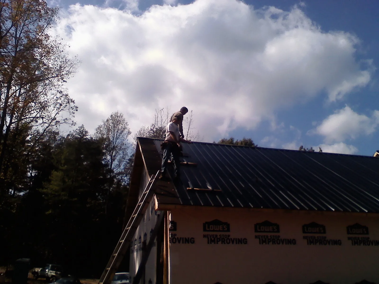 Roofer fastening dark metal panels high against a cloudy sky, from a Roof Inspection job in Poolesville